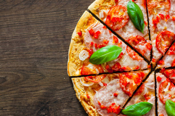 istock sliced Pizza with Mozzarella cheese, Ham, Tomatoes, pepper, Spices and Fresh Basil. Italian pizza on wooden background. 1074238992
