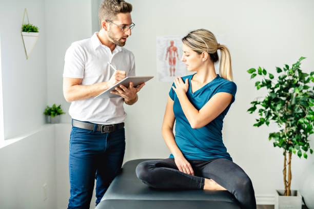 un moderno uomo di fisioterapia riabilitativa al lavoro con la clientela donna parla di problema alla spalla - patient doctor male talking foto e immagini stock