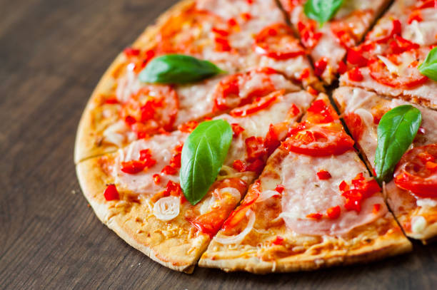 istock sliced Pizza with Mozzarella cheese, Ham, Tomatoes, pepper, Spices and Fresh Basil. Italian pizza on wooden background. 1074239206