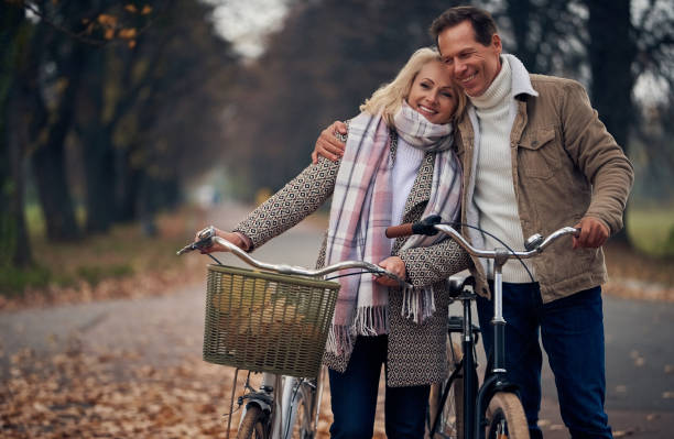 pareja senior en el parque en otoño - action mature adult bicycle senior couple fotografías e imágenes de stock