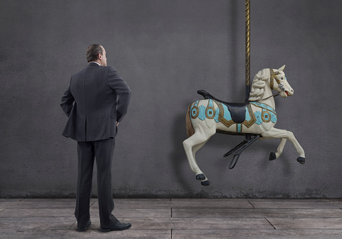 Rear view of businessman standing on wooden floor with carousel horse.