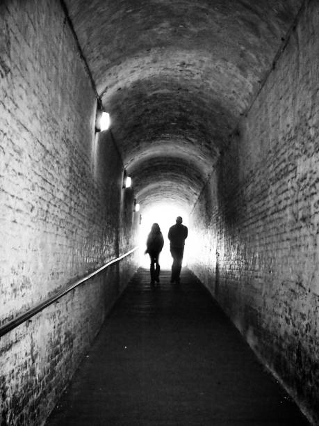 istock an old dark pedestrian tunnel with two unrecognisable people in silhouette against white light walking forwards 1074247620