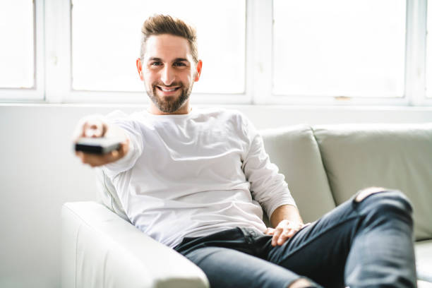 istock A Happy young man sitting with TV remote control on a couch at home 1074250482