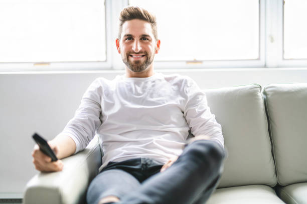 istock A Happy young man sitting with TV remote control on a couch at home 1074250496