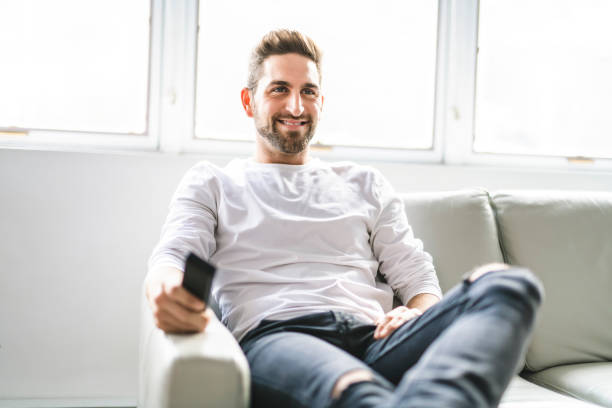 istock A Happy young man sitting with TV remote control on a couch at home 1074250506