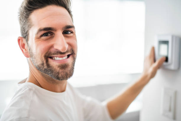 istock A Cheerful man set the thermostat at house 1074250582