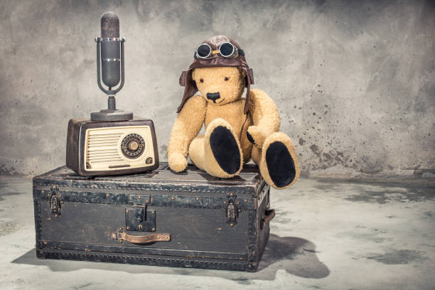 retro radio, studio microphone, teddy bear toy with leather aviator's hat and goggles sitting on old aged classic travel trunk circa 1900s. broadcasting concept. vintage style filtered photo - aviator glasses audio imagens e fotografias de stock