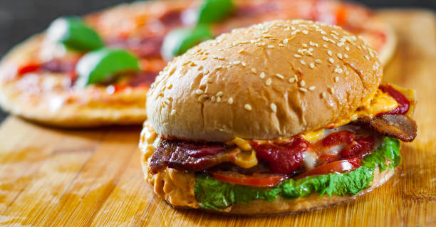 istock bacon cheese burger with beef patty tomato onion and Pizza with Mozzarella cheese, Ham, Tomatoes, salami, pepper, pepperoni Spices and Fresh Basil 1074255142