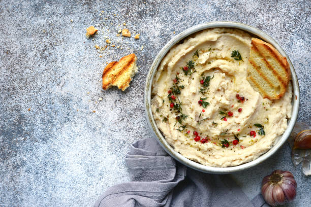 White bean hummus with baked garlic and dried herbs White bean hummus with baked garlic and dried herbs in a bowl over grey slate, stone or concrete background.Top view with copy space. lebanese culture stock pictures, royalty-free photos & images