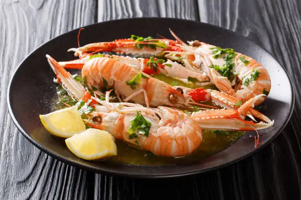 Freshly cooked langoustines, scampi with lemon and tasty sauce with herbs close-up on a plate on a black table. horizontal