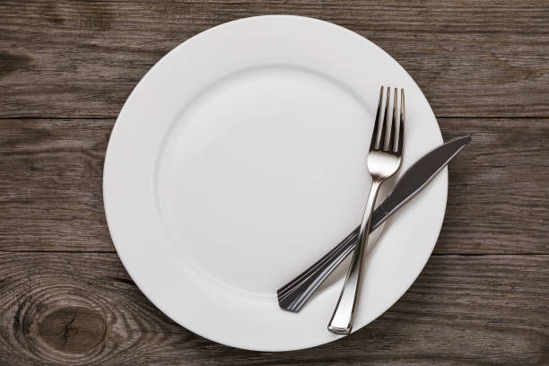 istock Empty white ceramic plate and cutlery on wooden table, top view 1074282734