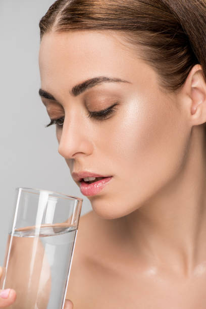 istock attractive young woman drinking water isolated on grey 1074286758