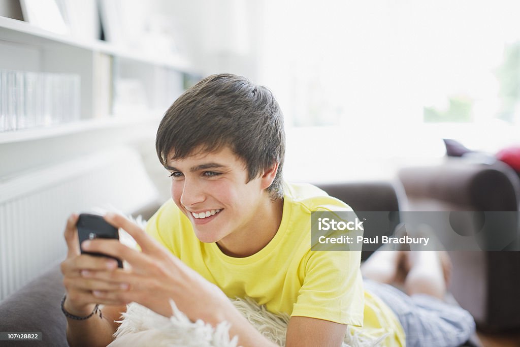 Sorridente ragazzo adolescente nel salotto di messaggi di testo - Foto stock royalty-free di Ragazzi adolescenti