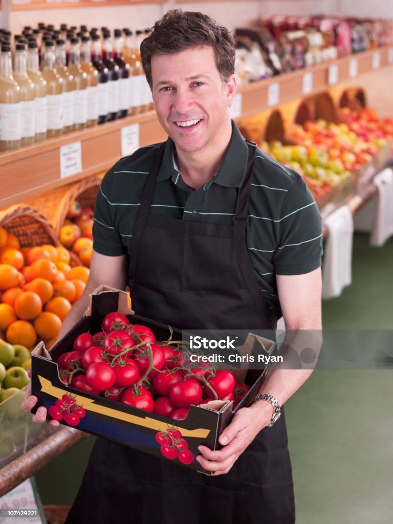 Trabajador sonriente sosteniendo Tomates en supermercado - Foto de stock de Fruta libre de derechos