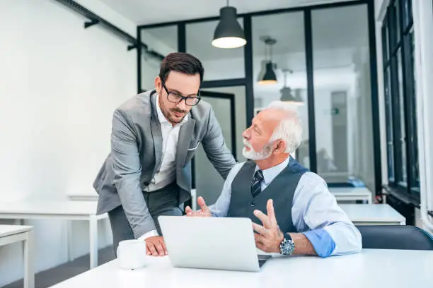 Photo of Young man discussing with boss or older employee in modern office.