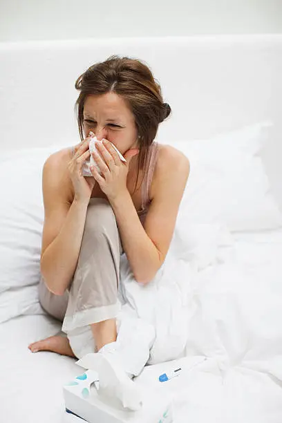 Photo of Sick woman in bed blowing nose