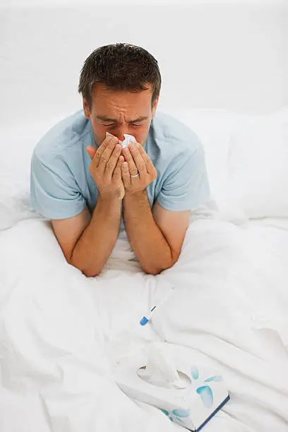 Photo of Sick man in bed blowing nose