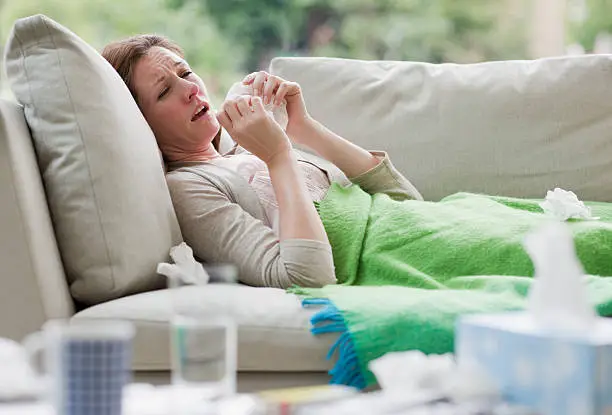 Photo of Sick woman laying on sofa blowing nose