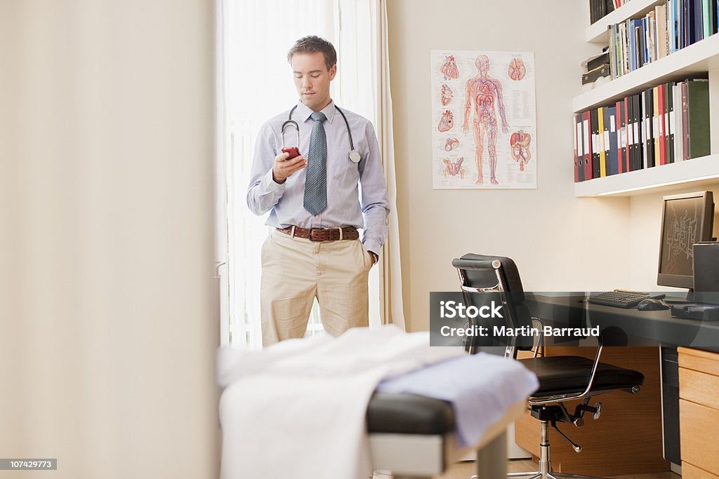 Médico usando teléfono celular en la oficina de médicos - Foto de stock de Doctor libre de derechos