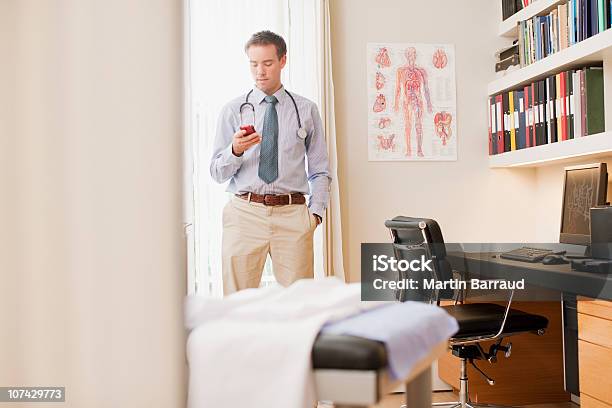 Médico Usando Teléfono Celular En La Oficina De Médicos Foto de stock y más banco de imágenes de Doctor