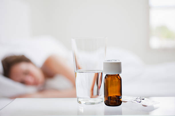 Close up of pill bottle with sick woman in background  sleeping pill stock pictures, royalty-free photos & images
