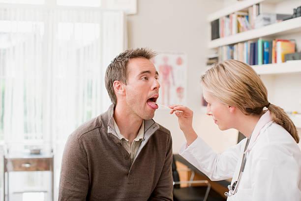 medico esaminando i pazienti gola in ufficio medici - mettere fuori la lingua foto e immagini stock
