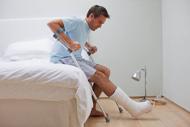 uomo con una gamba rotta cercando di alzarsi dal letto - clothing uncertainty household equipment brown hair foto e immagini stock