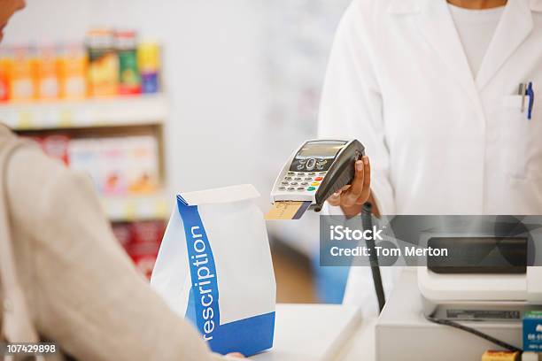 Farmacista Con Dispositivo Di Sicurezza Di Un Farmaco Per Il Cliente In Negozio - Fotografie stock e altre immagini di Farmacia