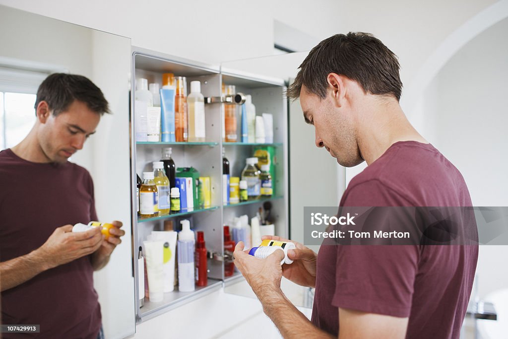 Homem olhando em garrafas de armário de banheiro - Foto de stock de Armário de Banheiro royalty-free