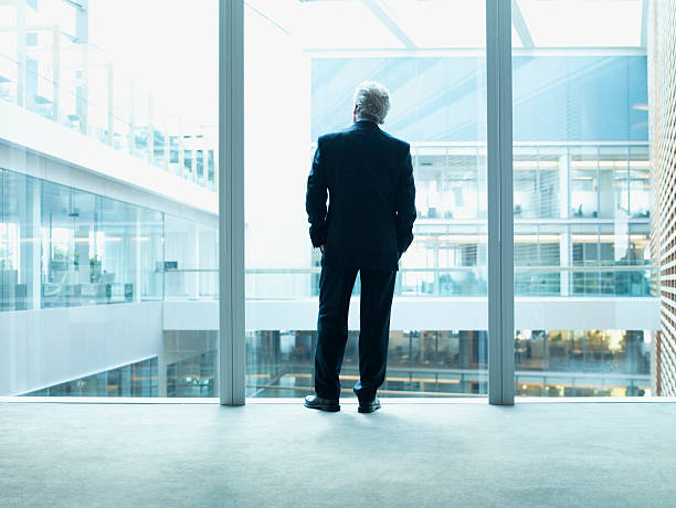 hombre de negocios mirando a través de la pared de vidrio en la oficina - full length windows fotografías e imágenes de stock