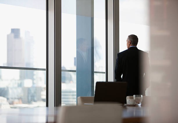 businessman looking out conference room window - autoriteit stockfoto's en -beelden