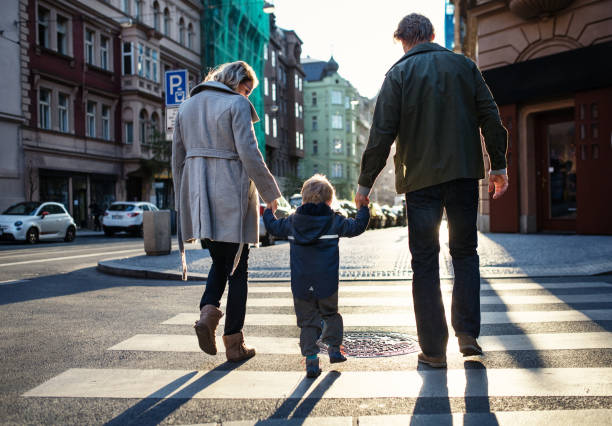 una vista trasera del niño pequeño niño con padres cruzar un camino al aire libre en la ciudad. - familia de cruzar la calle fotografías e imágenes de stock