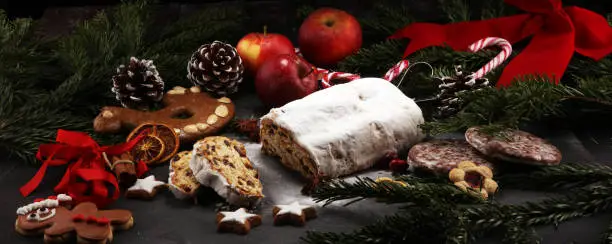 Traditional European Christmas pastry, fragrant home baked stollen, with spices and dried fruit. Sliced on rustic table with xmas tree branches and decorations.