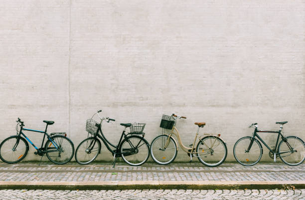 Four bicycles stand near a white brick wall. Several different bikes parked along an empty street in Copenhagen.