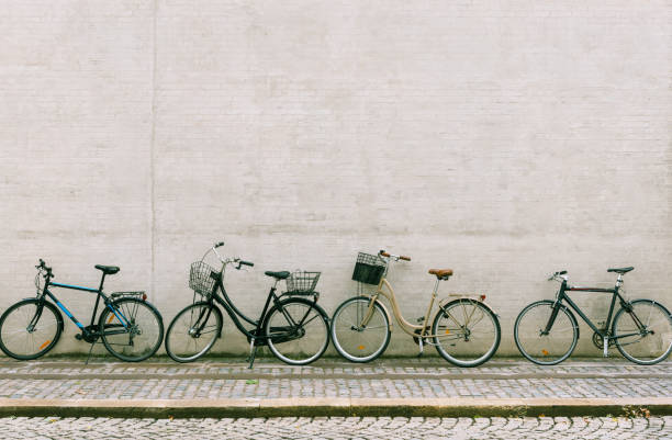 cztery rowery stoją w pobliżu białej ceglanej ściany. kilka różnych rowerów zaparkowanych wzdłuż pustej ulicy w kopenhadze - denmark copenhagen brick street zdjęcia i obrazy z banku zdjęć