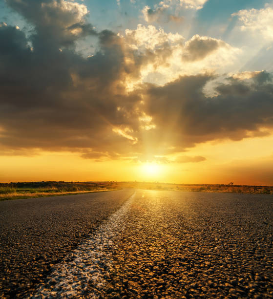 istock orange sunset in low dark dramatic clouds over asphalt road 1074369266