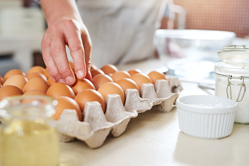 Cropped shot of a woman reaching for an egg to use while baking at home