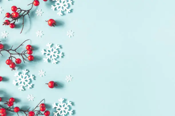 Photo of Christmas or winter composition. Frame made of snowflakes and red berries on pastel blue background. Christmas, winter, new year concept. Flat lay, top view, copy space