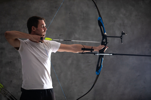 Male archer aiming with bow and arrow on gray background