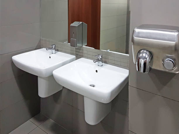 istock Bathroom interior in light beige and white colors. Round ceramic washbasins. Mirrors, plastic soap dish and chrome faucets for washing hands after a toilet. Design with dark facing tiles. 1074436242
