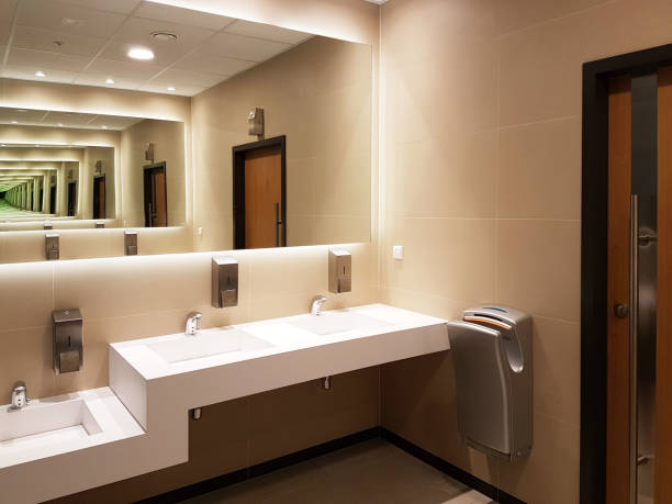 istock Bathroom interior in light beige and white colors. Round ceramic washbasins. Mirrors, plastic soap dish and chrome faucets for washing hands after a toilet. Design with dark facing tiles. 1074436270