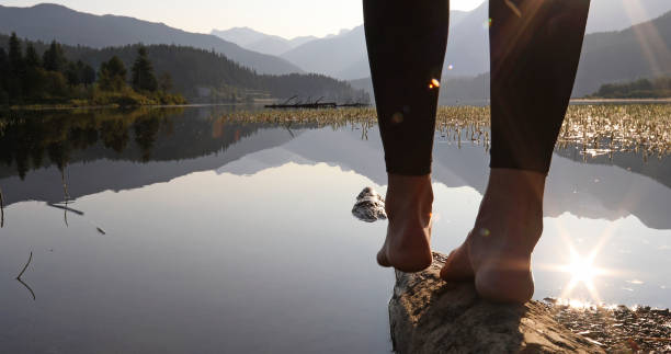 Woman's feet balance on log, at lake