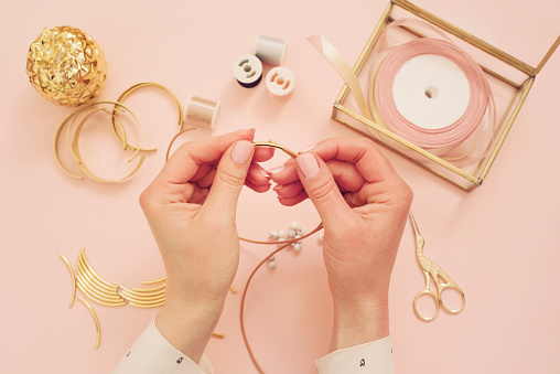 Trabajo de diseñador de joyería. Mujer manos haciendo joyería hecha a mano. Espacio de trabajo de feminidad freelance de moda de estilo plano laico. Oro y rosa pastel photo
