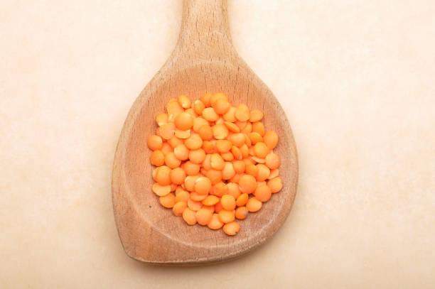 Red lentils on wooden spoon and brown background