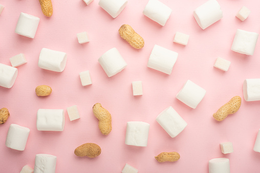 White marshmallows, with pieces of sugar, and nuts on a pink background. The ability to use as a background, the concept of the concept of winter food. Flyte lay or on top.
