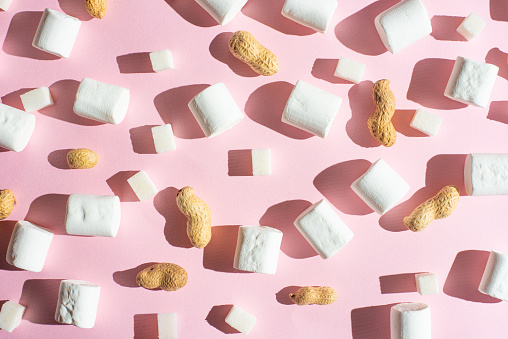 White marshmallows, with pieces of sugar, and nuts on a pink background, with hard shadows. The ability to use as a background, the concept of the concept of winter food. Flyte lay or on top.
