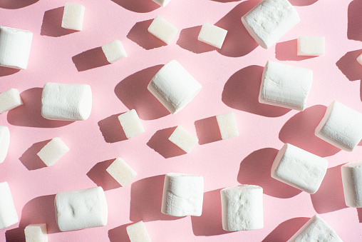 White marshmallows, with sugar cubes, on a pink background, with hard shadows. The ability to use as a background, the concept of the concept of winter food. Flyte lay or on top.