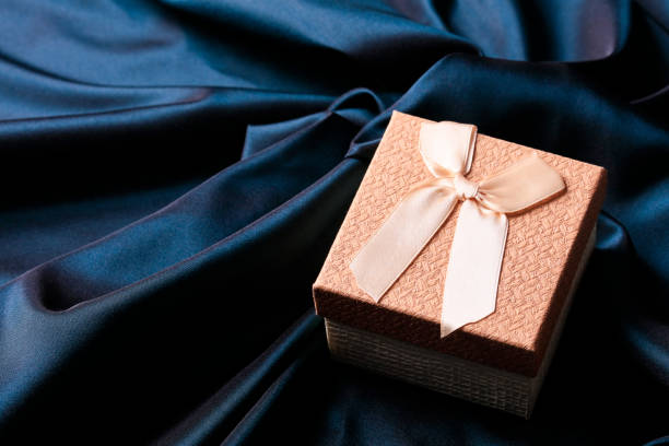 Golden gift box on navy blue satin background Golden gift box on navy blue satin background luxury craft stock pictures, royalty-free photos & images