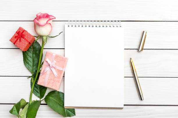 istock Blank notepad with beautiful rose and gift boxes on white wooden table. 1074520960