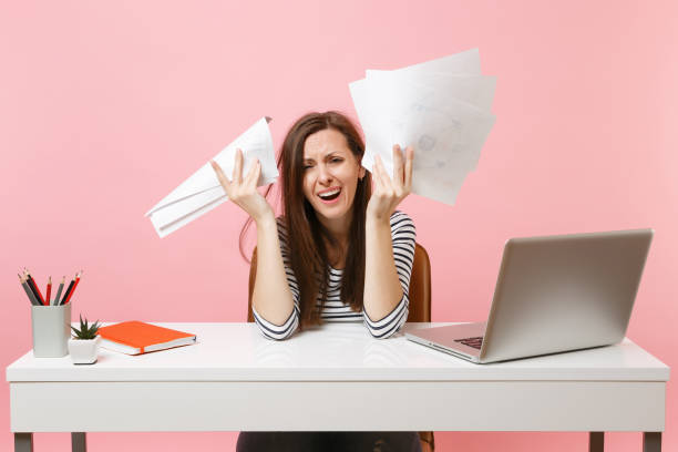 istock Frustrated woman in desperation crying spreading hand hold paper documents work on project while sit at office with laptop isolated on pink background. Achievement business career concept. Copy space. 1074526488